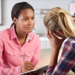 A woman speaks to a young adult in a clinical setting