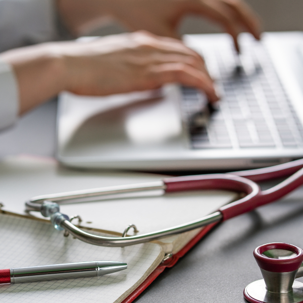 Doctor sat typing on computer at desk.